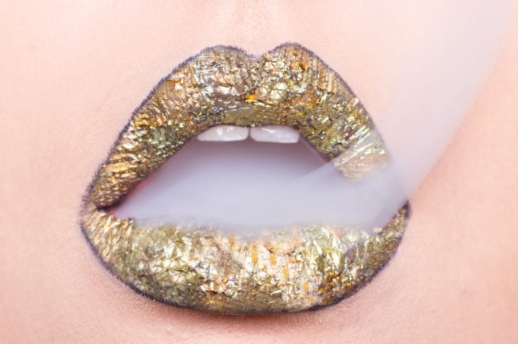 Smoke escapes gold painted lips.