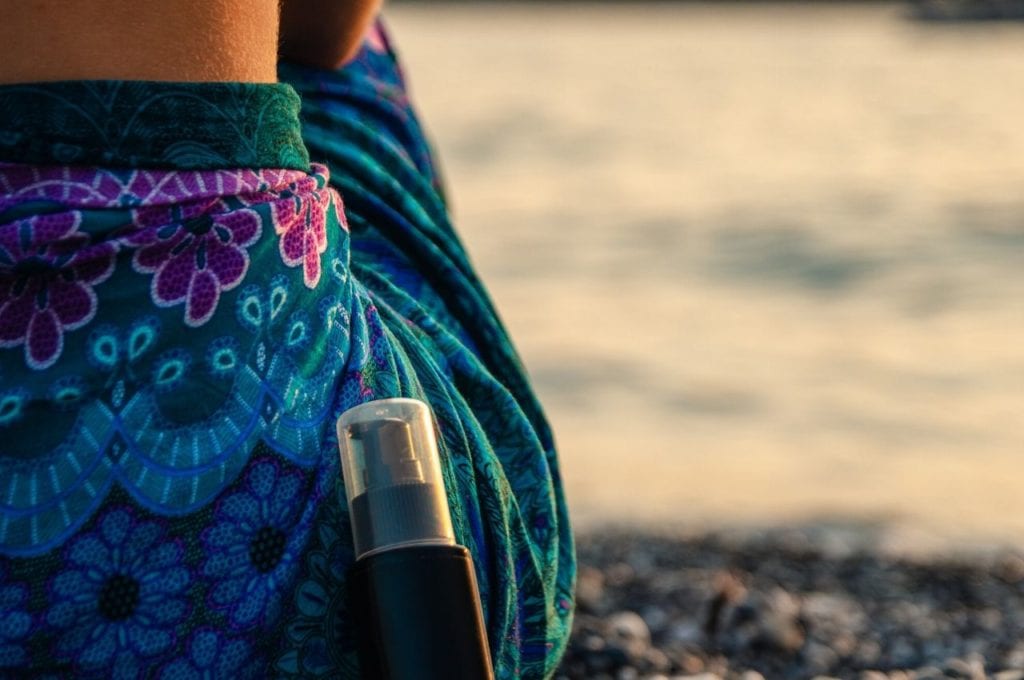 Body cream bottle rests on woman's body on a rocky shore.