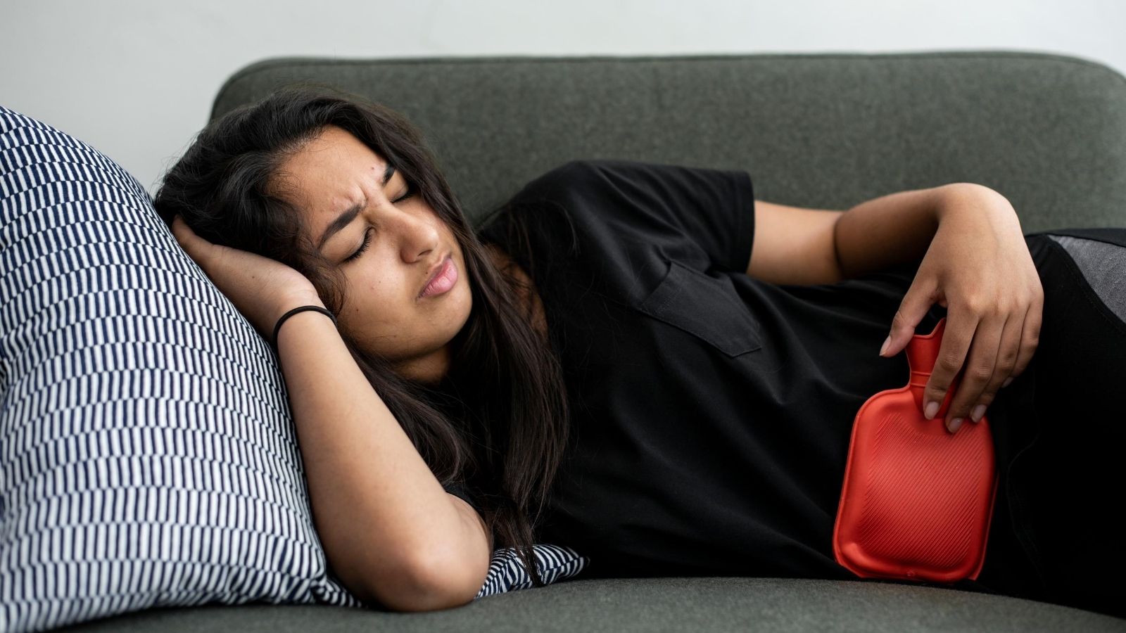 A woman with stomach pain resting on the couch with a hot water bottle