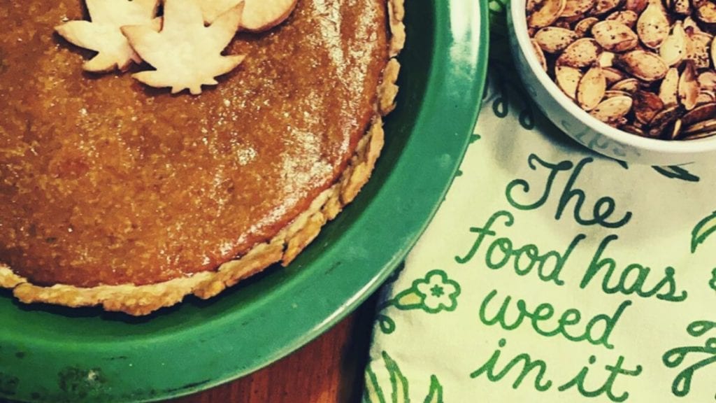 A cannabis pumpkin pie next to a tea towel that warns that the food has weed in it.