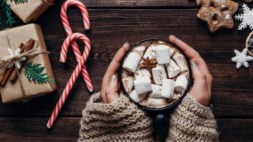 A pair of hands holding a warm cup of cacao topped with marshmallows.