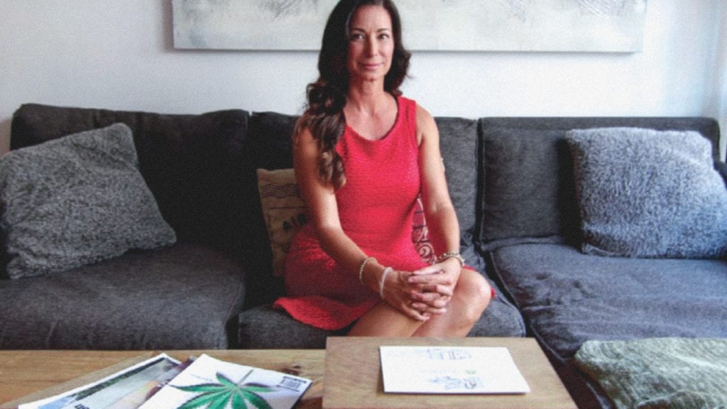 A photograph of Rosy Mondin sitting on a couch in front of a coffee table with documents about cannabis.