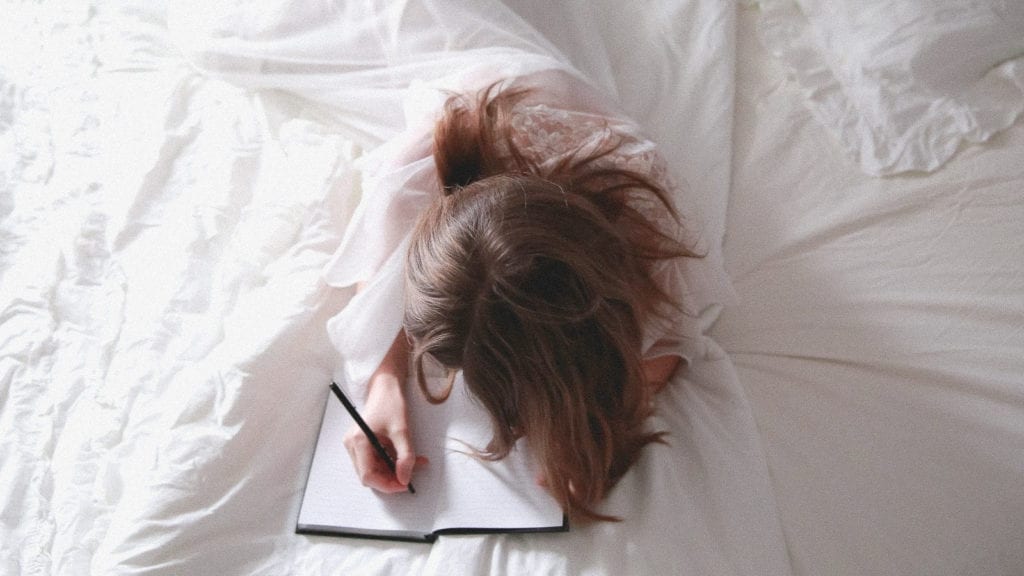 A photograph of a woman journaling on her bed