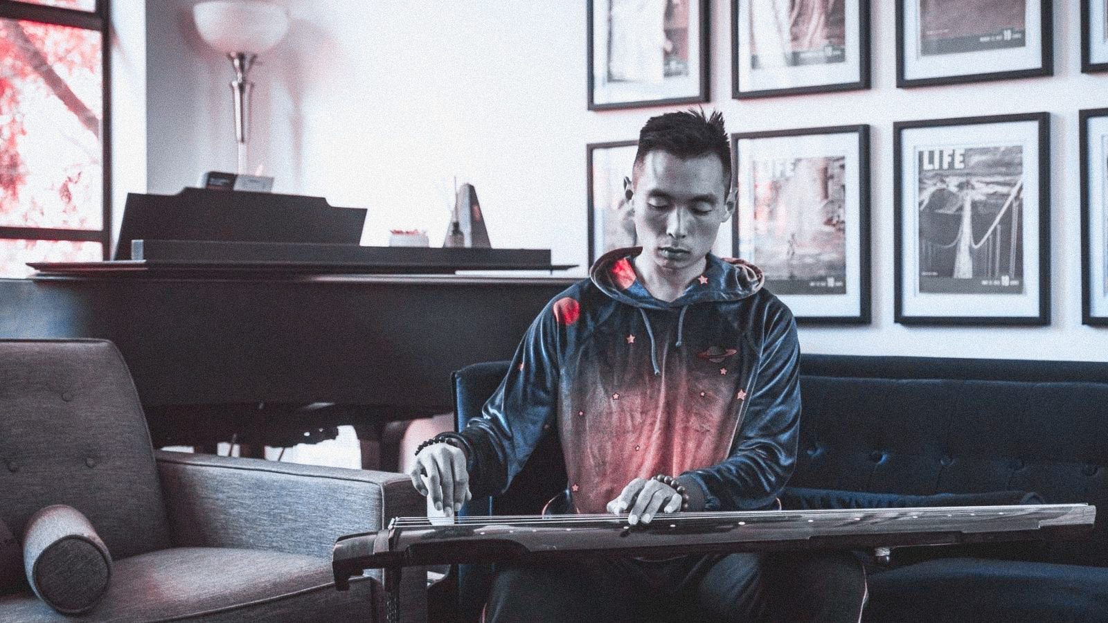 A photograph of Justin Zhu playing the ghuzeng, a traditional Chinese instrument in his San Francisco apartment.