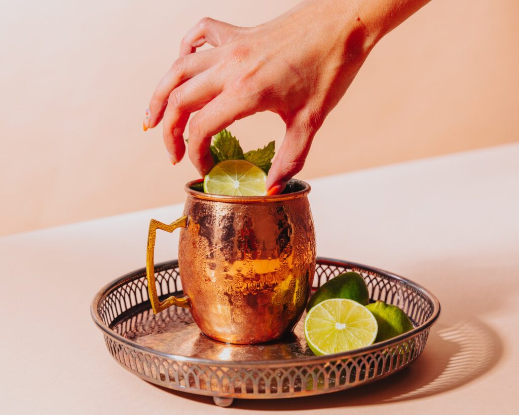 A photograph of a hand dipping a lime slice into a copper mug full of kombucha mule for an article on cannabis mocktail recipes